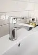 Waschtischarmatur aus Chrom von Ideal Standard mit einem Hebelgriff, montiert auf einer weißen Oberfläche, im Hintergrund helle Wandfliesen und dekorative Fläschchen.